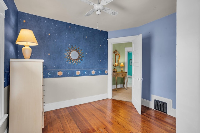 unfurnished room with visible vents, wallpapered walls, an accent wall, baseboards, and hardwood / wood-style flooring