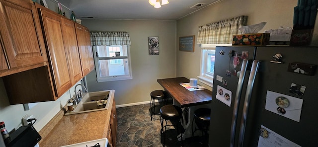 kitchen featuring visible vents, brown cabinets, stone finish floor, a sink, and freestanding refrigerator