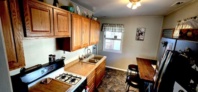 kitchen with visible vents, freestanding refrigerator, a sink, white gas range oven, and stone finish flooring