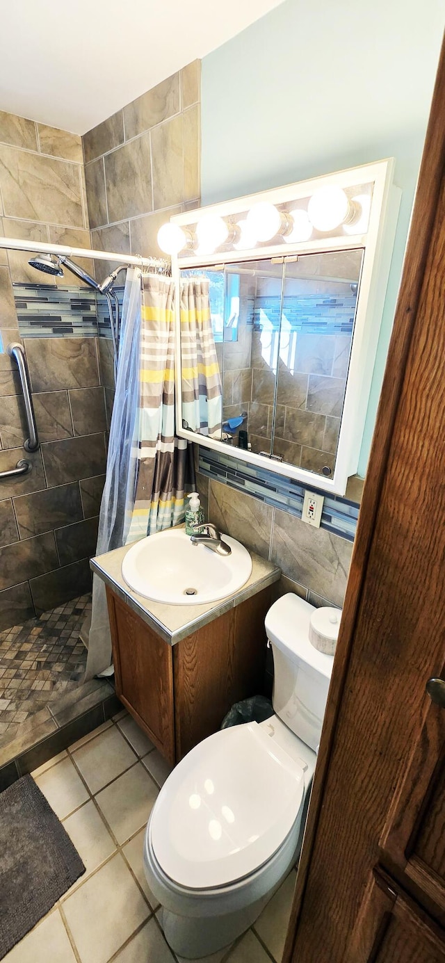 full bath with tile patterned flooring, toilet, vanity, a stall shower, and tile walls