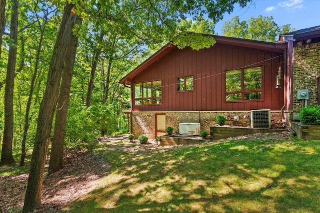 view of property exterior featuring cooling unit, a lawn, and brick siding