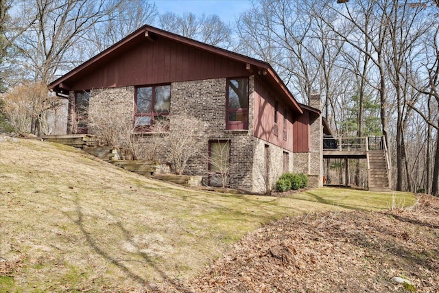 view of side of home featuring brick siding, stairs, a chimney, a deck, and a yard