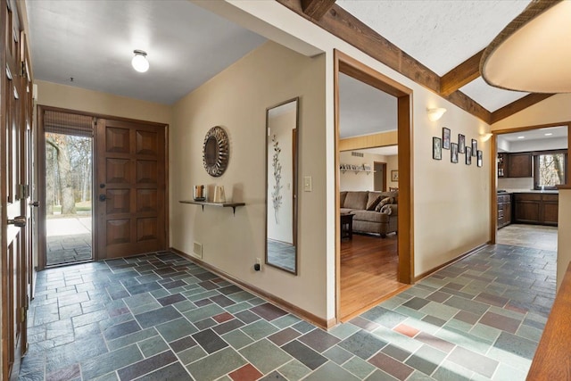 entrance foyer with vaulted ceiling with beams, visible vents, baseboards, and stone tile flooring