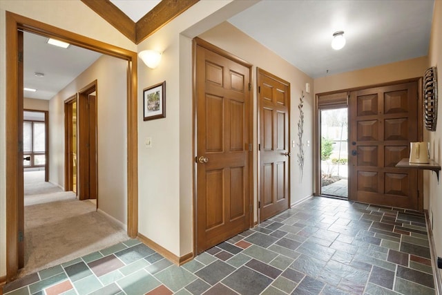 foyer featuring stone tile floors, dark carpet, and baseboards