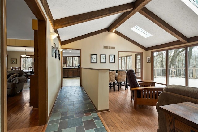 interior space featuring beamed ceiling, visible vents, a textured ceiling, dark wood finished floors, and a skylight