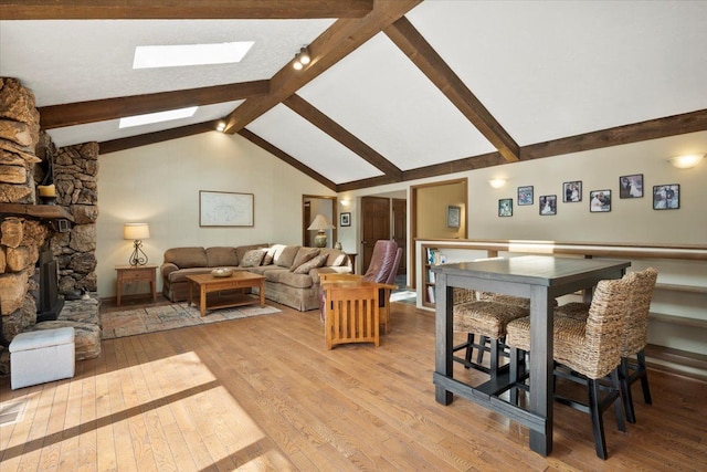 dining area with beam ceiling, high vaulted ceiling, light wood-style flooring, a stone fireplace, and a skylight