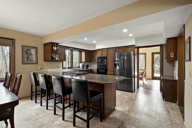 kitchen with a breakfast bar area, a peninsula, dark brown cabinets, stainless steel refrigerator with ice dispenser, and black microwave