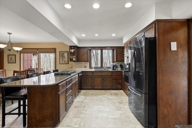 kitchen with stainless steel gas cooktop, a breakfast bar, recessed lighting, black fridge, and a sink