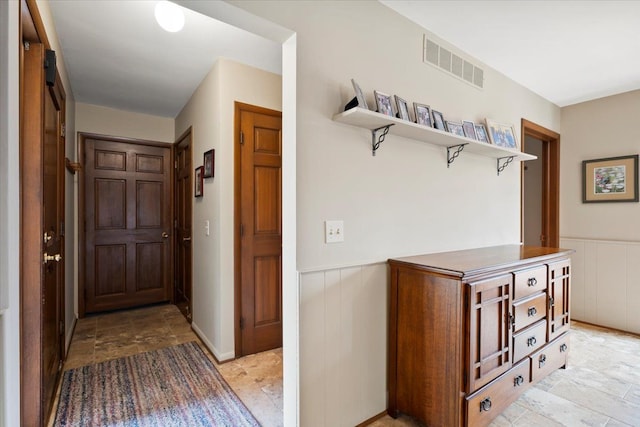 corridor with stone finish floor, visible vents, and wainscoting