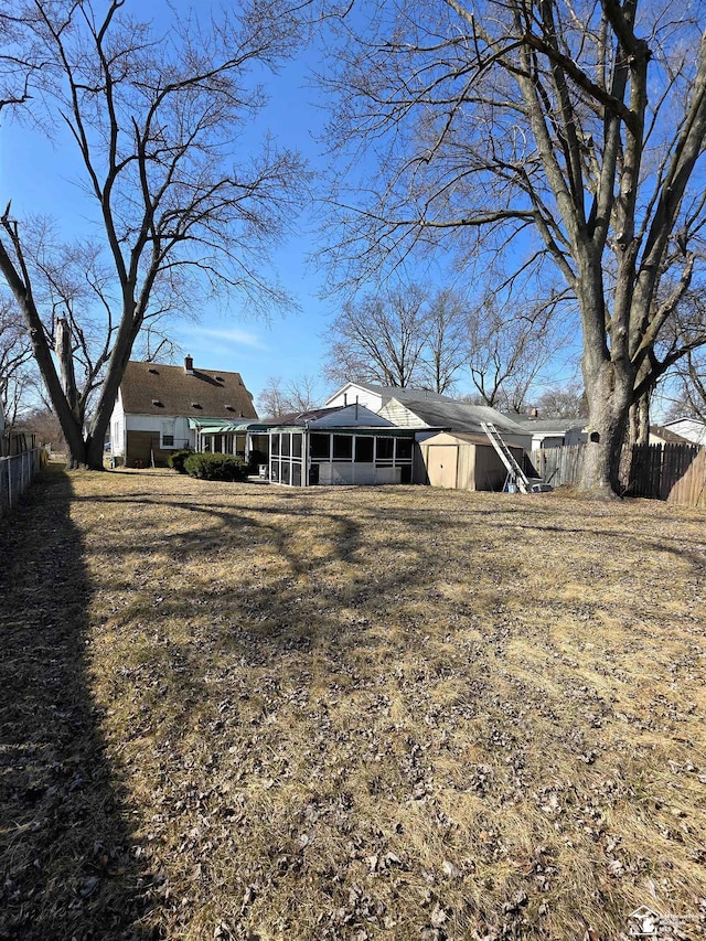 rear view of house with a storage unit, fence, an outdoor structure, and a sunroom