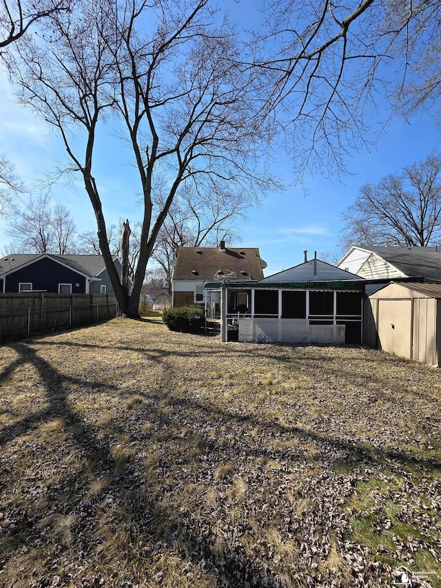 back of house featuring fence, a storage shed, an outdoor structure, and a sunroom