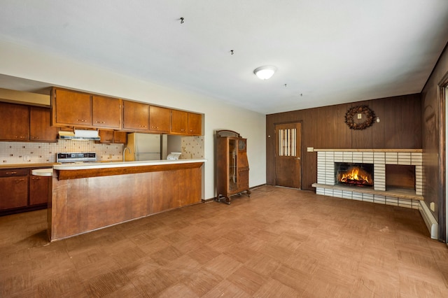 kitchen featuring a brick fireplace, open floor plan, brown cabinets, freestanding refrigerator, and stove