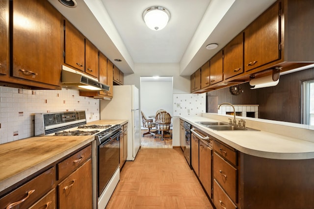 kitchen with gas stove, a sink, light countertops, under cabinet range hood, and backsplash