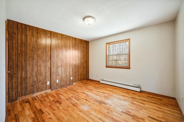 unfurnished room with a baseboard radiator, wood finished floors, and wood walls