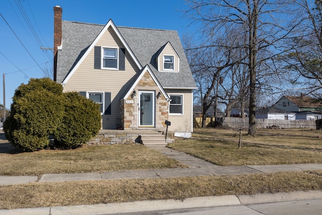 view of front of property featuring fence, roof with shingles, a chimney, a front lawn, and stone siding