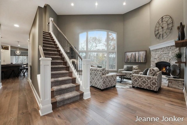 living area featuring hardwood / wood-style floors, a high ceiling, recessed lighting, a stone fireplace, and stairs