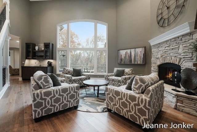 living area with a stone fireplace, a towering ceiling, and wood-type flooring