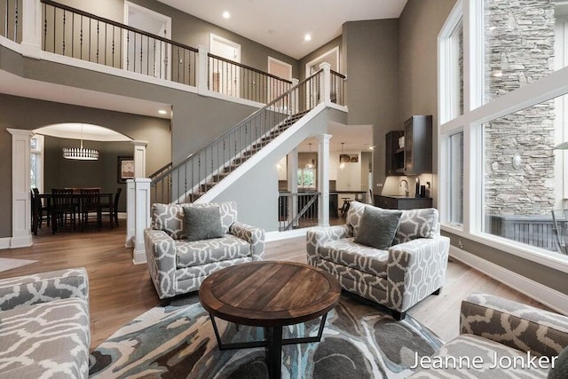 living room with arched walkways, a high ceiling, ornate columns, and wood finished floors