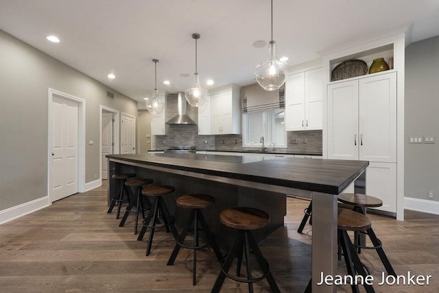 kitchen with a center island, dark wood finished floors, white cabinets, wall chimney exhaust hood, and a sink