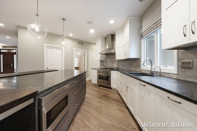 kitchen featuring visible vents, a sink, stainless steel appliances, light wood-style floors, and wall chimney range hood