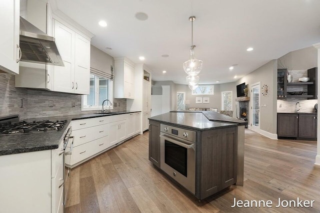 kitchen featuring dark countertops, cooktop, wall chimney range hood, and stainless steel oven