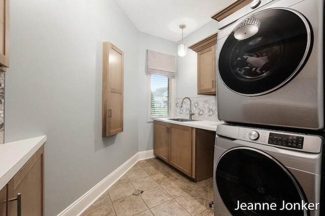 clothes washing area with baseboards, light tile patterned flooring, cabinet space, a sink, and stacked washer and clothes dryer