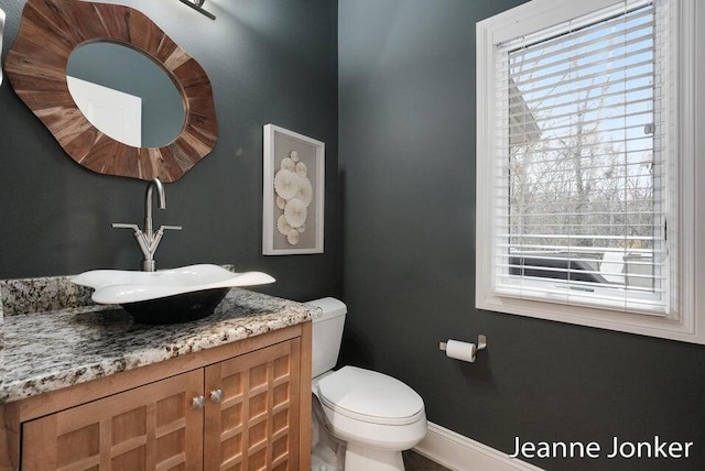 half bath with baseboards, toilet, and vanity