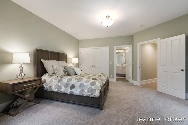 carpeted bedroom featuring a closet, ensuite bath, and baseboards