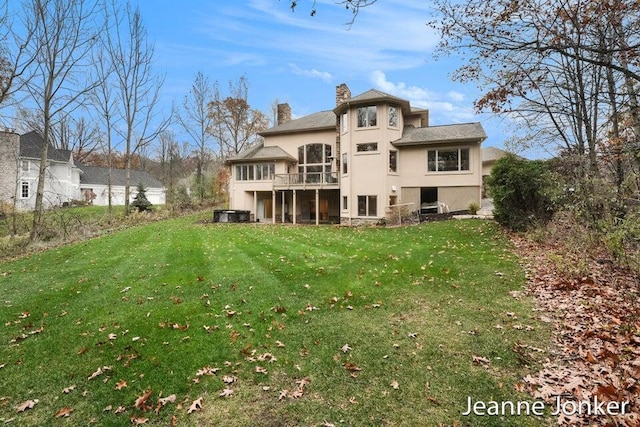 rear view of house with stucco siding, a lawn, and a chimney