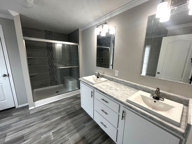 bathroom featuring a shower stall, wood finished floors, crown molding, and a sink