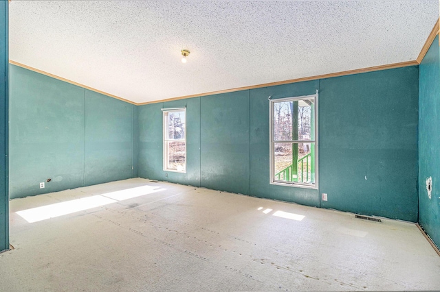 empty room featuring visible vents, a textured ceiling, and ornamental molding