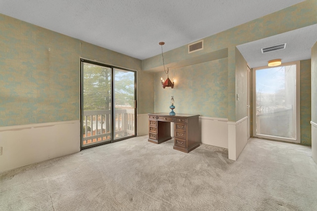 unfurnished office featuring wallpapered walls, a textured ceiling, visible vents, and light carpet