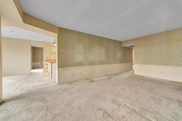 carpeted empty room featuring wallpapered walls and a textured ceiling