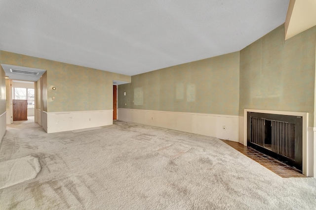 unfurnished living room featuring a fireplace with flush hearth, wainscoting, visible vents, and carpet floors