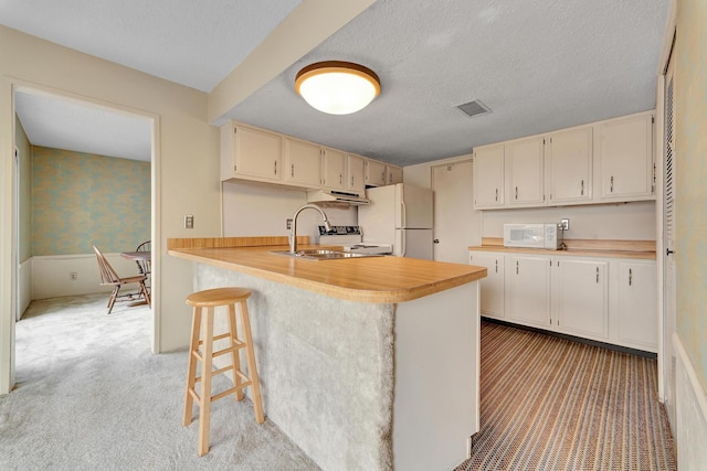 kitchen featuring visible vents, wallpapered walls, light countertops, white appliances, and a sink