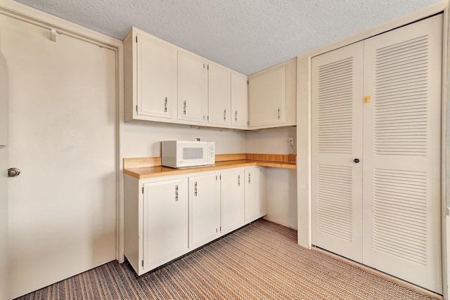 kitchen featuring white microwave, carpet flooring, white cabinets, and a textured ceiling