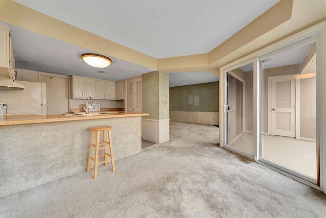 kitchen with a peninsula, freestanding refrigerator, a sink, light carpet, and a kitchen breakfast bar