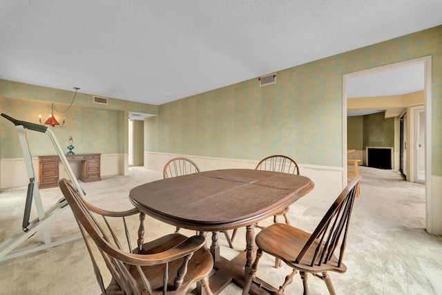 dining area featuring visible vents, light colored carpet, a wainscoted wall, and a textured ceiling