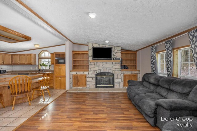 living room featuring light wood-style floors, crown molding, a fireplace, and a textured ceiling