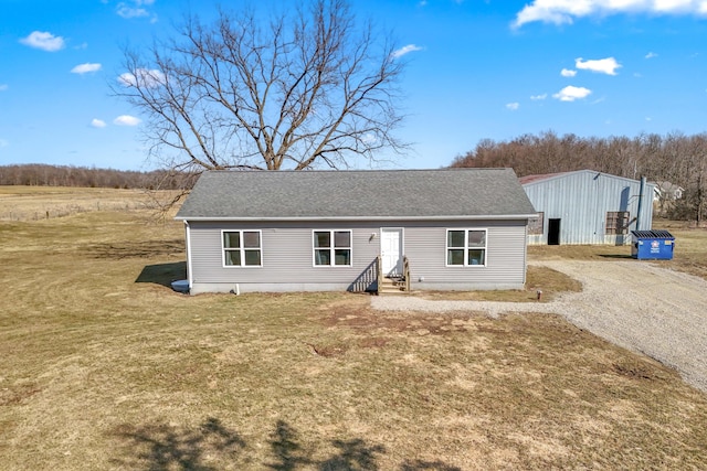 view of front of property with entry steps, gravel driveway, a front lawn, and roof with shingles