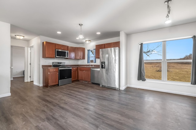 kitchen featuring decorative light fixtures, a sink, dark wood-style floors, stainless steel appliances, and baseboards