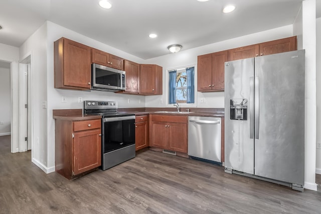 kitchen with a sink, dark countertops, dark wood-style floors, and stainless steel appliances