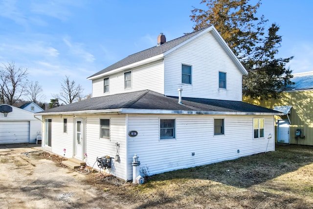 rear view of house featuring a detached garage, entry steps, a chimney, an outdoor structure, and driveway