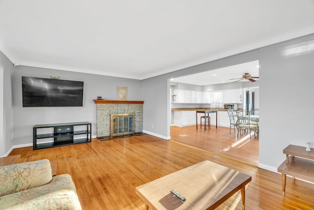 living area with a ceiling fan, baseboards, a fireplace with flush hearth, recessed lighting, and light wood-type flooring