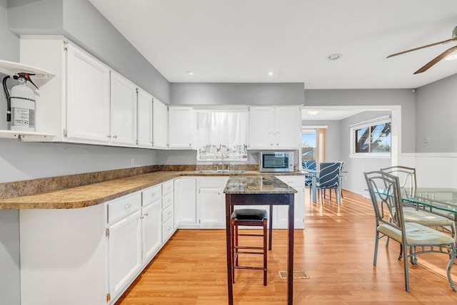 kitchen with light wood-type flooring, open shelves, stainless steel microwave, white cabinets, and ceiling fan