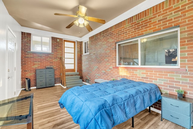 bedroom with ceiling fan, wood finished floors, and brick wall