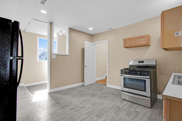 kitchen featuring baseboards, light wood-type flooring, freestanding refrigerator, light countertops, and stainless steel gas stove