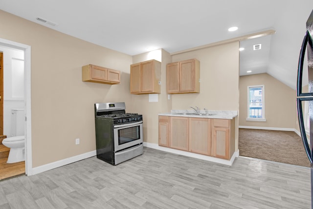 kitchen featuring gas range, light brown cabinets, light countertops, and a sink