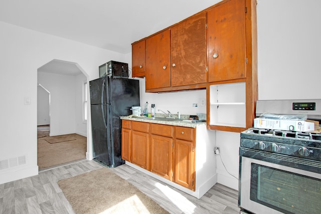 kitchen with brown cabinetry, visible vents, a sink, black appliances, and light countertops