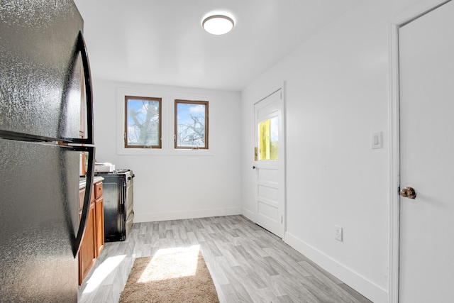 kitchen featuring light wood finished floors, brown cabinetry, freestanding refrigerator, and baseboards